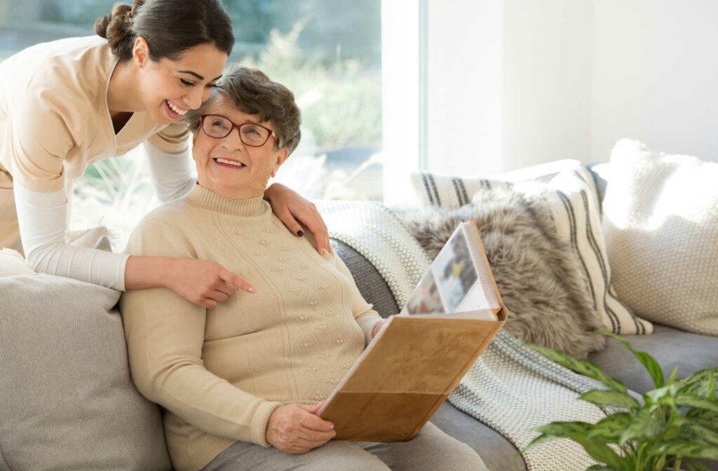 A skilled caregiver is helping an elderly woman deal with her memory loss as she goes through old photos on an album held in her hand.