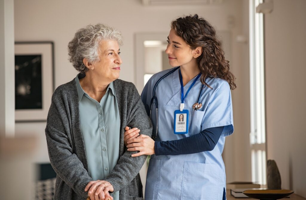 A young nurse and a senior woman smiling at each other.