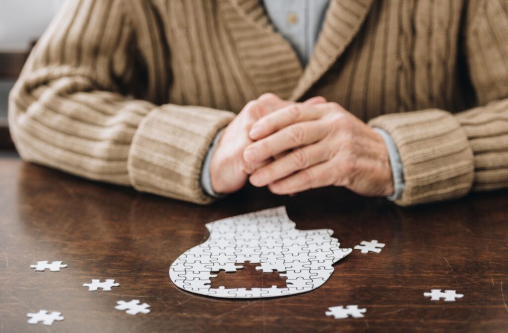 Cropped view of senior man playing with puzzles on table.