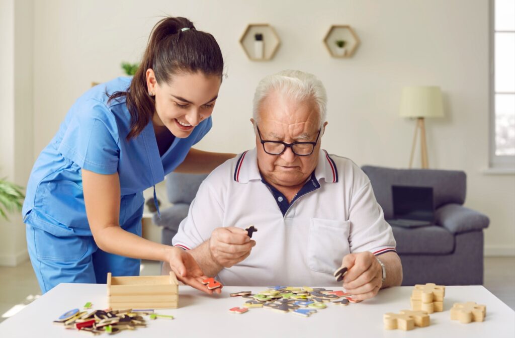 A caregiver helps an older adult with a puzzle game sitting a table in a community living facility