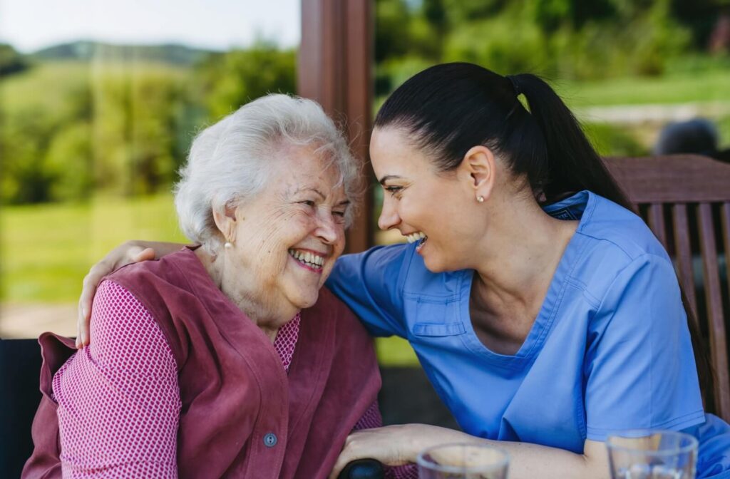 Smiling elderly woman sitting outdoors with her caregiver, sharing a joyful moment together.