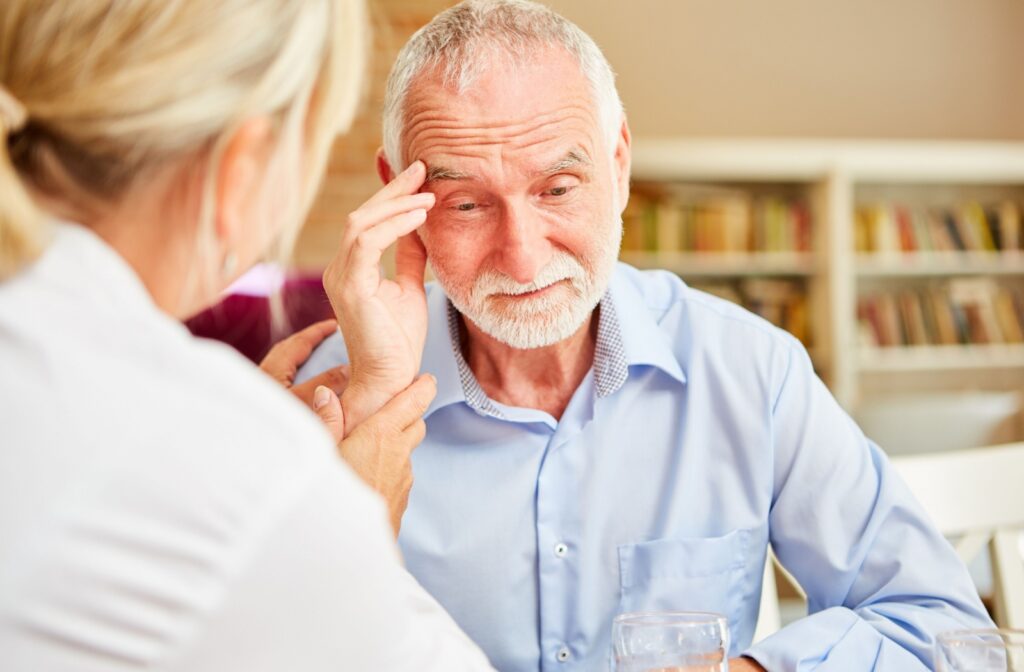 An older adult rubbing their forehead and trying to remember something while talking with a nurse.