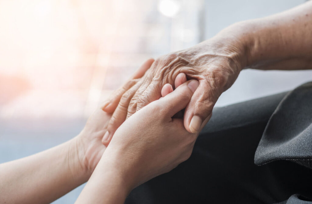 A caregiver clasping the hand of an older adult with Alzheimer's disease.