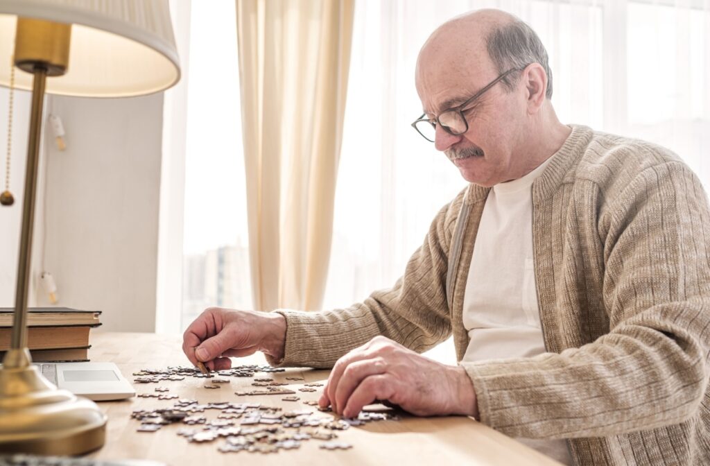 A senior carefully considers pieces of a jigsaw puzzle when starting the puzzle on their desk in a well-lit room