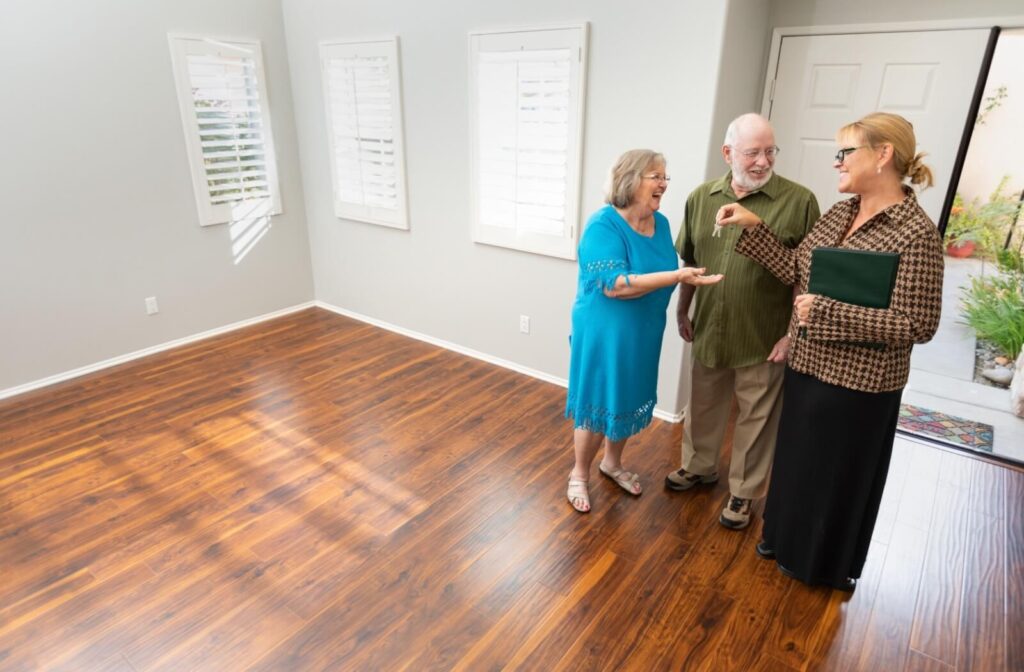 A representative of a senior living community turns over the keys to an older couple while they stand in an unfurnished living room